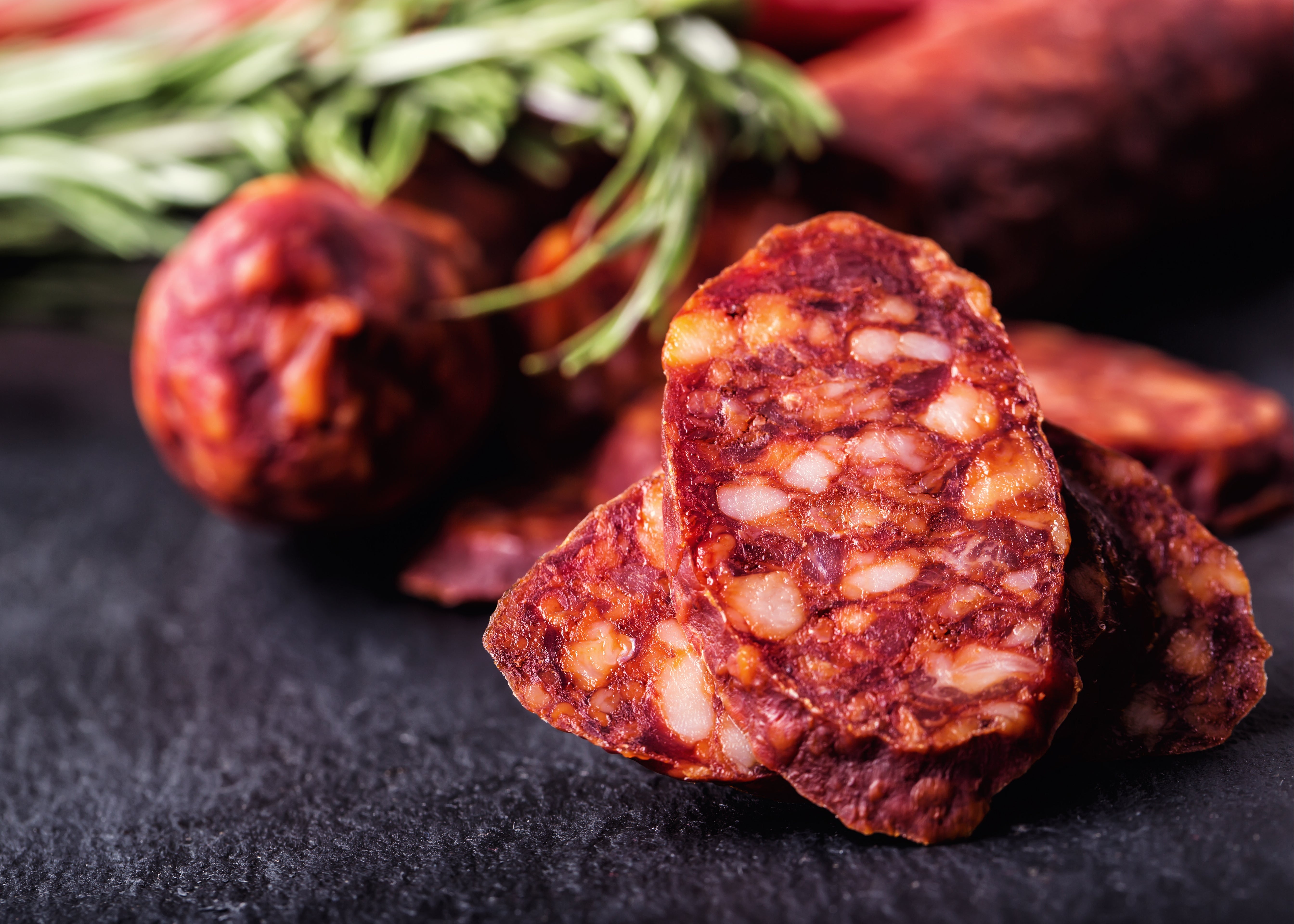 Sliced Futari chorizo on a dark surface with herbs in the background